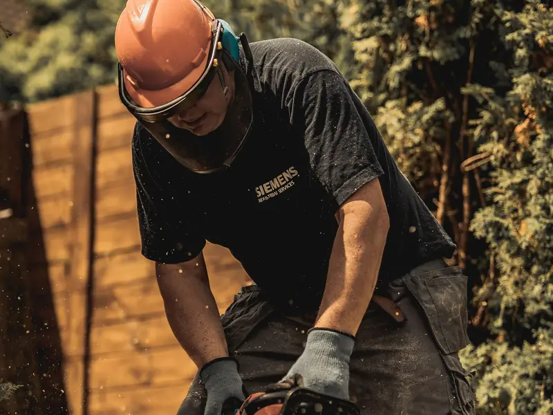 Crew member in a helmet and face guard cutting a log with a chainsaw