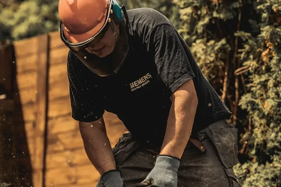Arborist in a helmet cutting a trunk with a chainsaw